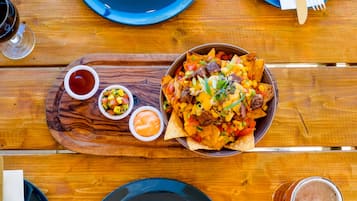 A wooden table with a bowl of nachos, a small bowl of salsa, and a glass of beer.