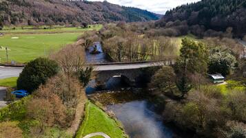 A bridge over a river with a path on the left and a green field in the background.