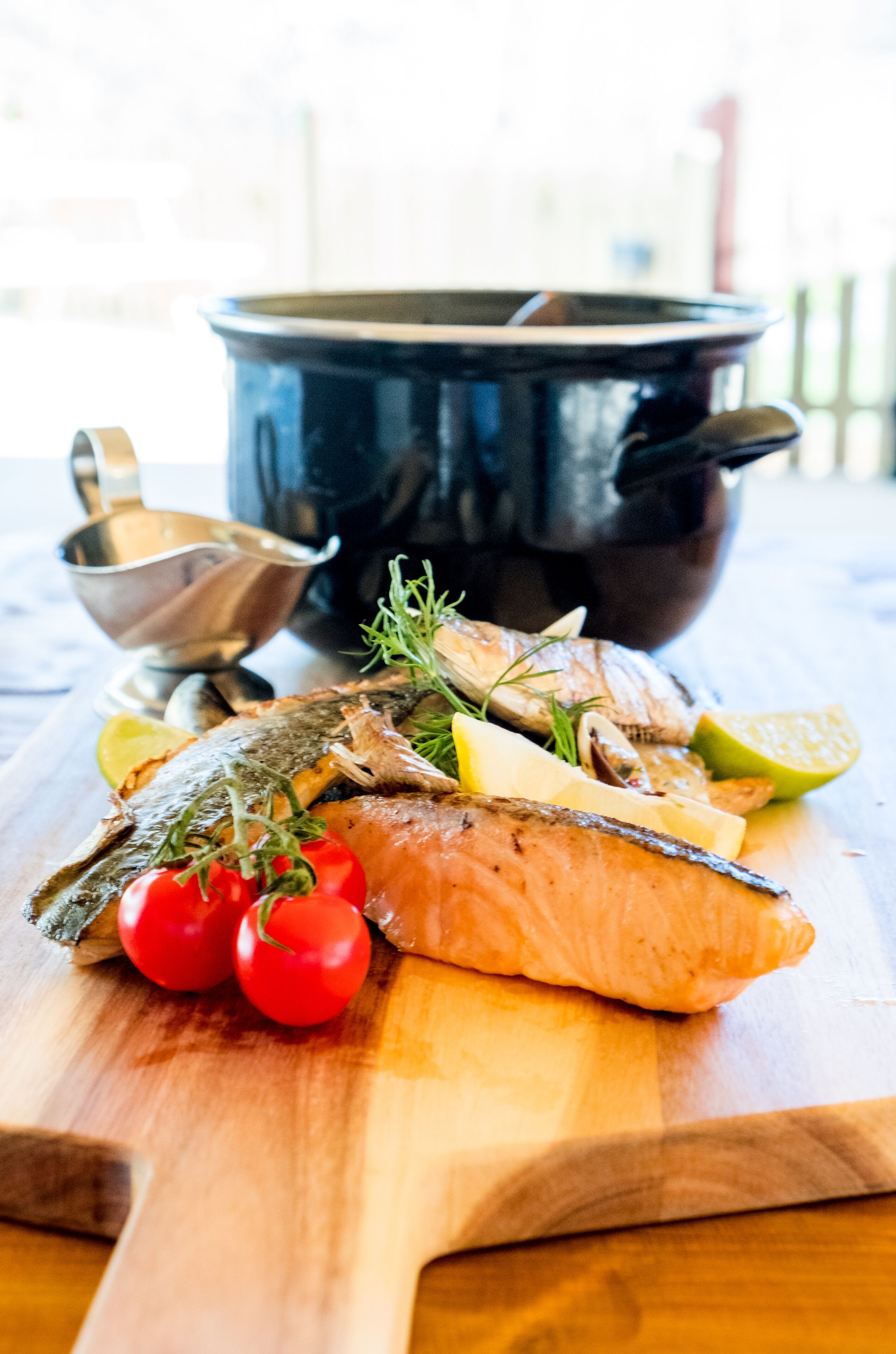 A wooden cutting board with a cooked fish, cherry tomatoes, and herbs.