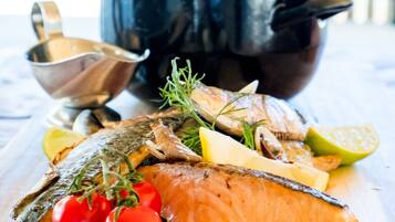 A wooden cutting board with a cooked fish, cherry tomatoes, and herbs.