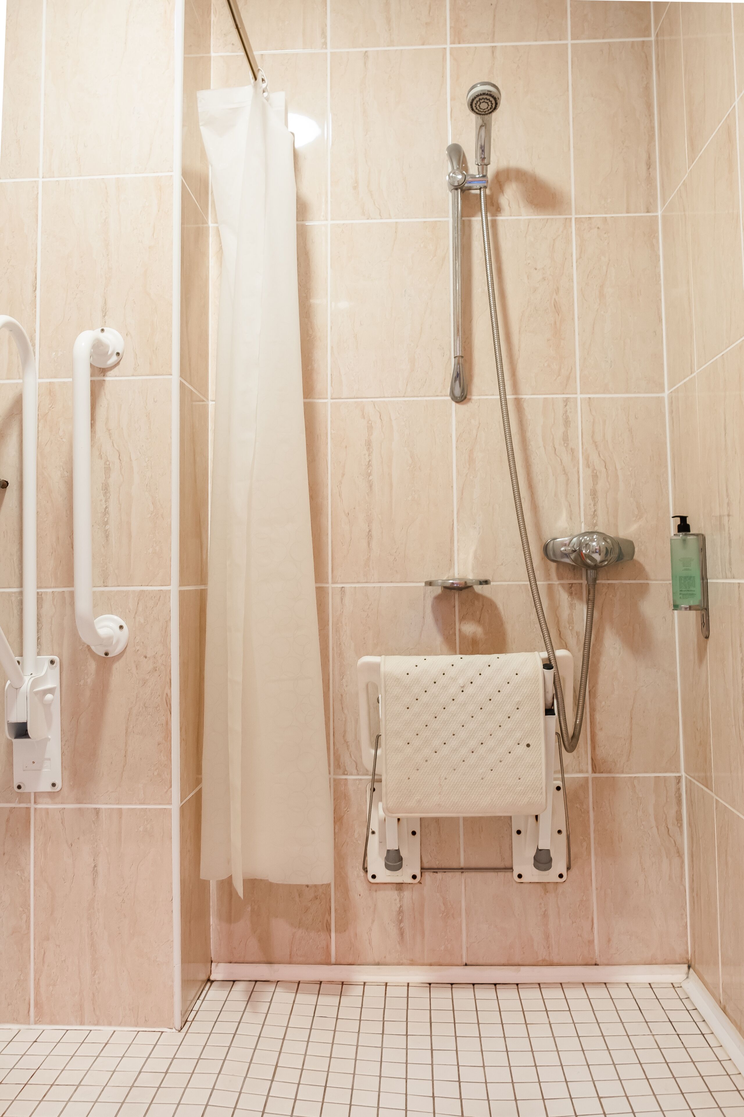 A shower area with a handheld showerhead, a wall-mounted faucet, and a handheld showerhead.