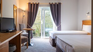 Habitación de hotel con cama, escritorio con televisor, una silla y balcón con cortinas.