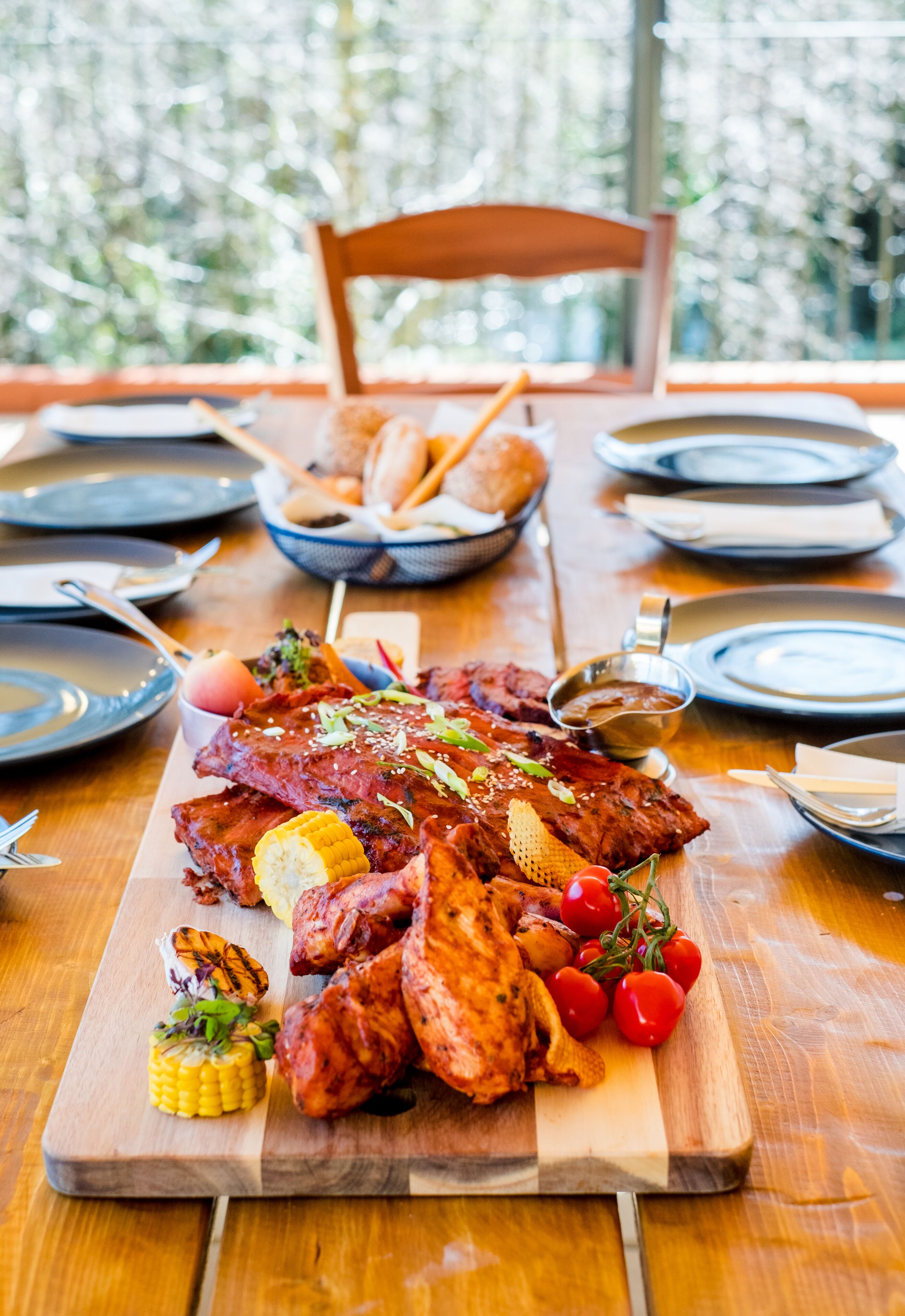 A wooden dining table with a large platter of grilled meats, vegetables, and bread.