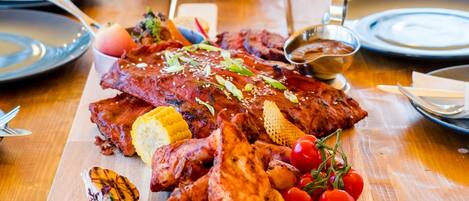 A wooden dining table with a large platter of grilled meats, vegetables, and bread.