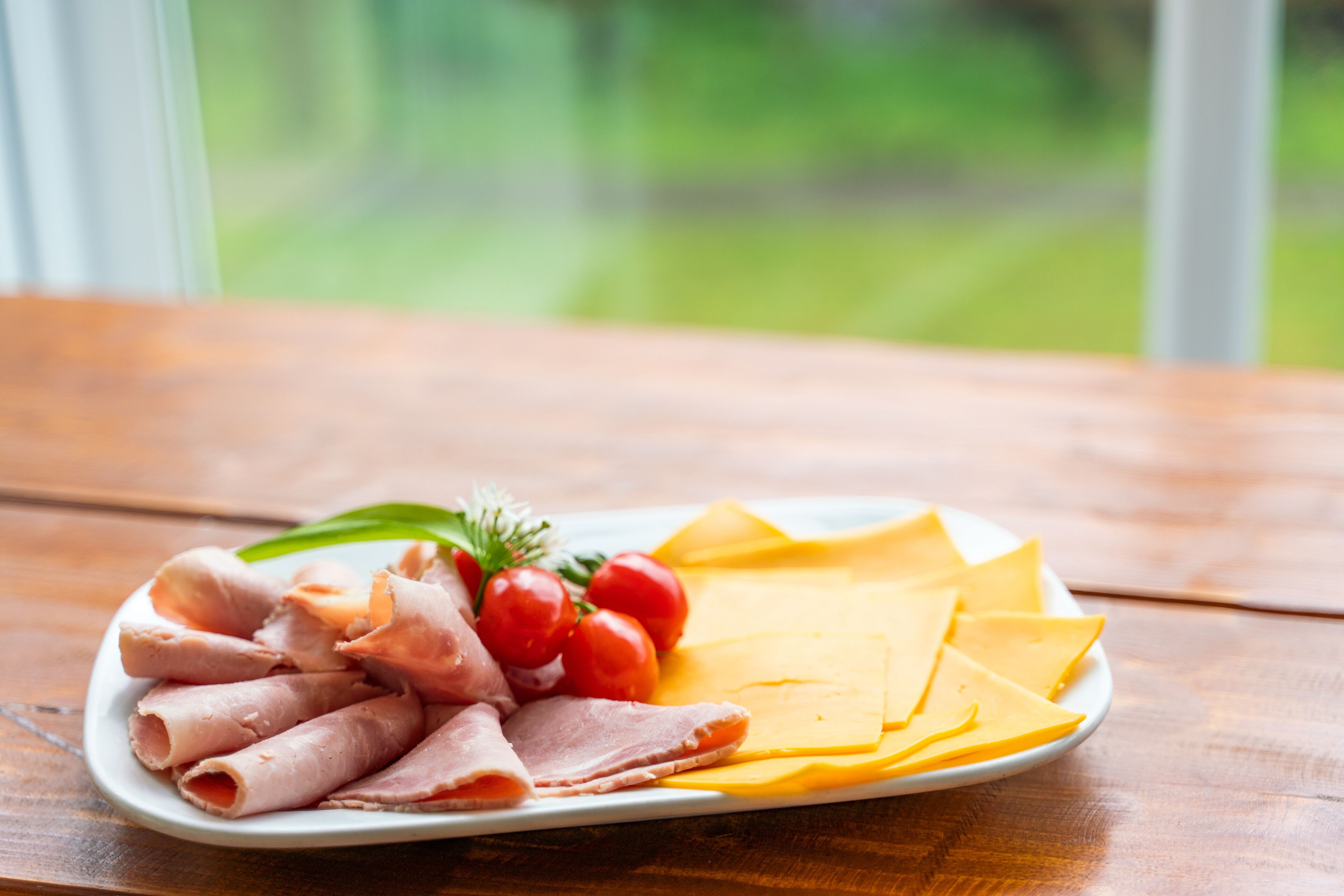 Une assiette de charcuteries et de fromages est posée sur une table en bois, avec une fenêtre en arrière-plan.