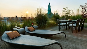 A rooftop terrace with lounge chairs, a table with chairs, and a view of a church spire. - Hotel Kö59 Düsseldorf - Member of Hommage Luxury Hotels Collection (Düsseldorf)