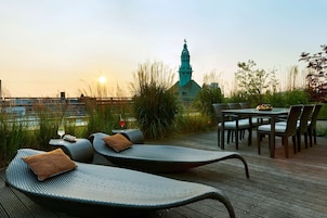 Una terraza en la azotea con sillones de descanso, una mesa y sillas, y vistas a la aguja de una iglesia.