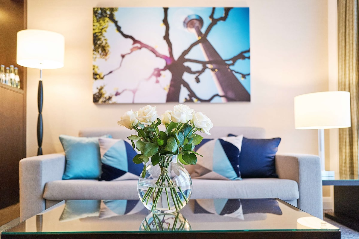 A modern living room with a glass coffee table, a vase of white flowers, and a sofa with blue cushions.
