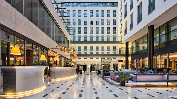 A modern hotel lobby with a central reception desk, seating areas, and a glass ceiling. - Hotel Kö59 Düsseldorf - Member of Hommage Luxury Hotels Collection (Düsseldorf)
