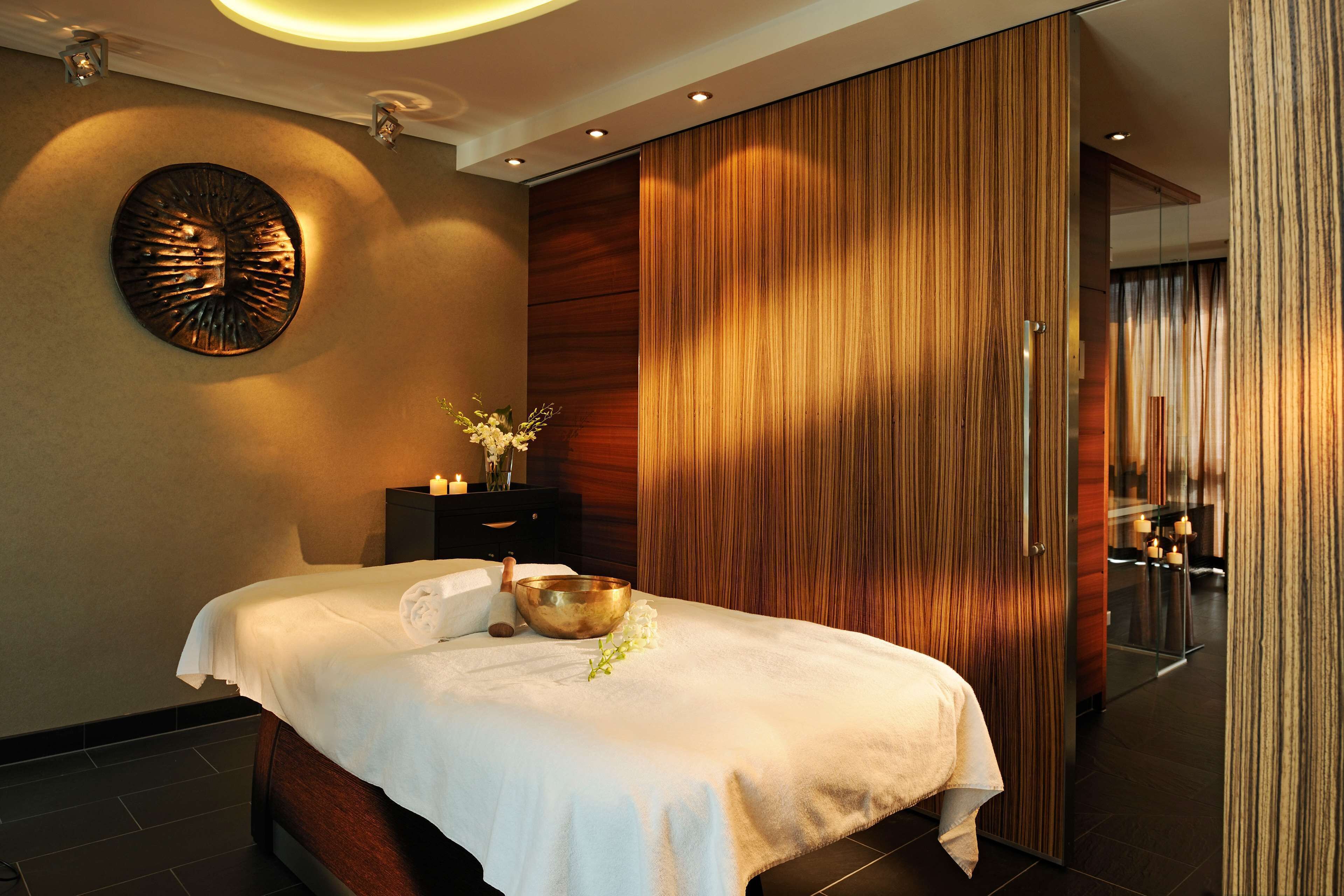 Un spa moderno con una cama, un panel de madera en la pared, un adorno mural y una mesita con vela y flores.