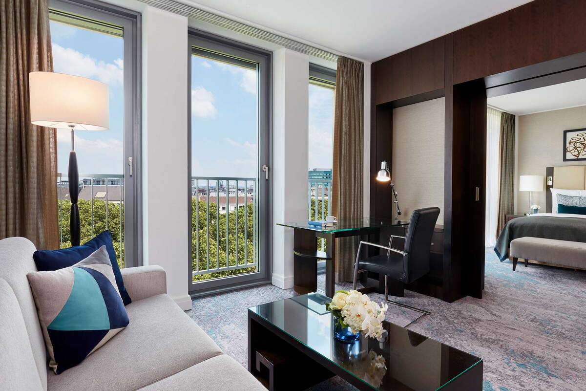 A hotel room with a sofa, a glass coffee table, a desk, and a bed.