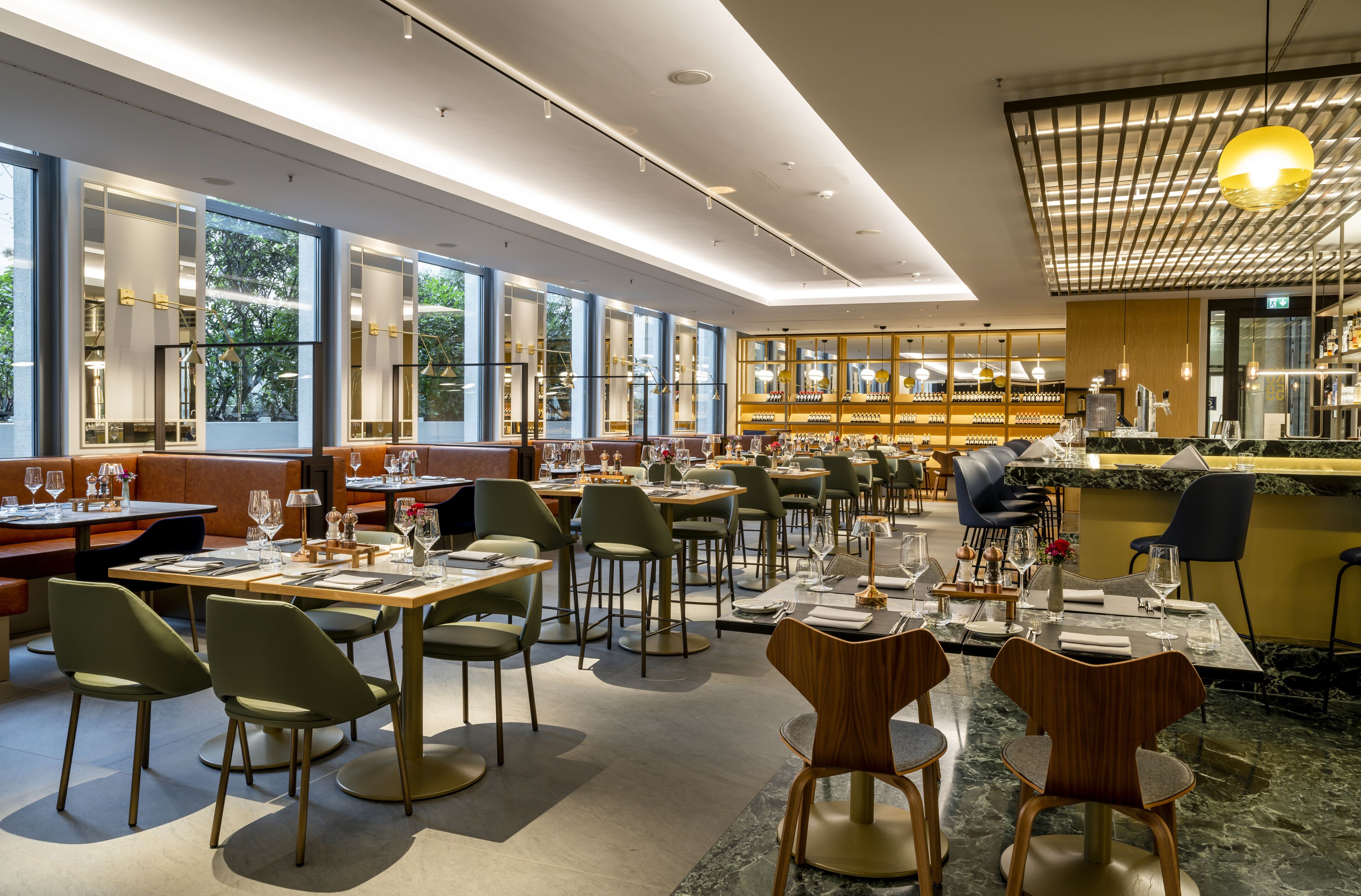 A modern restaurant with multiple dining tables and chairs, large windows, and a bar area.