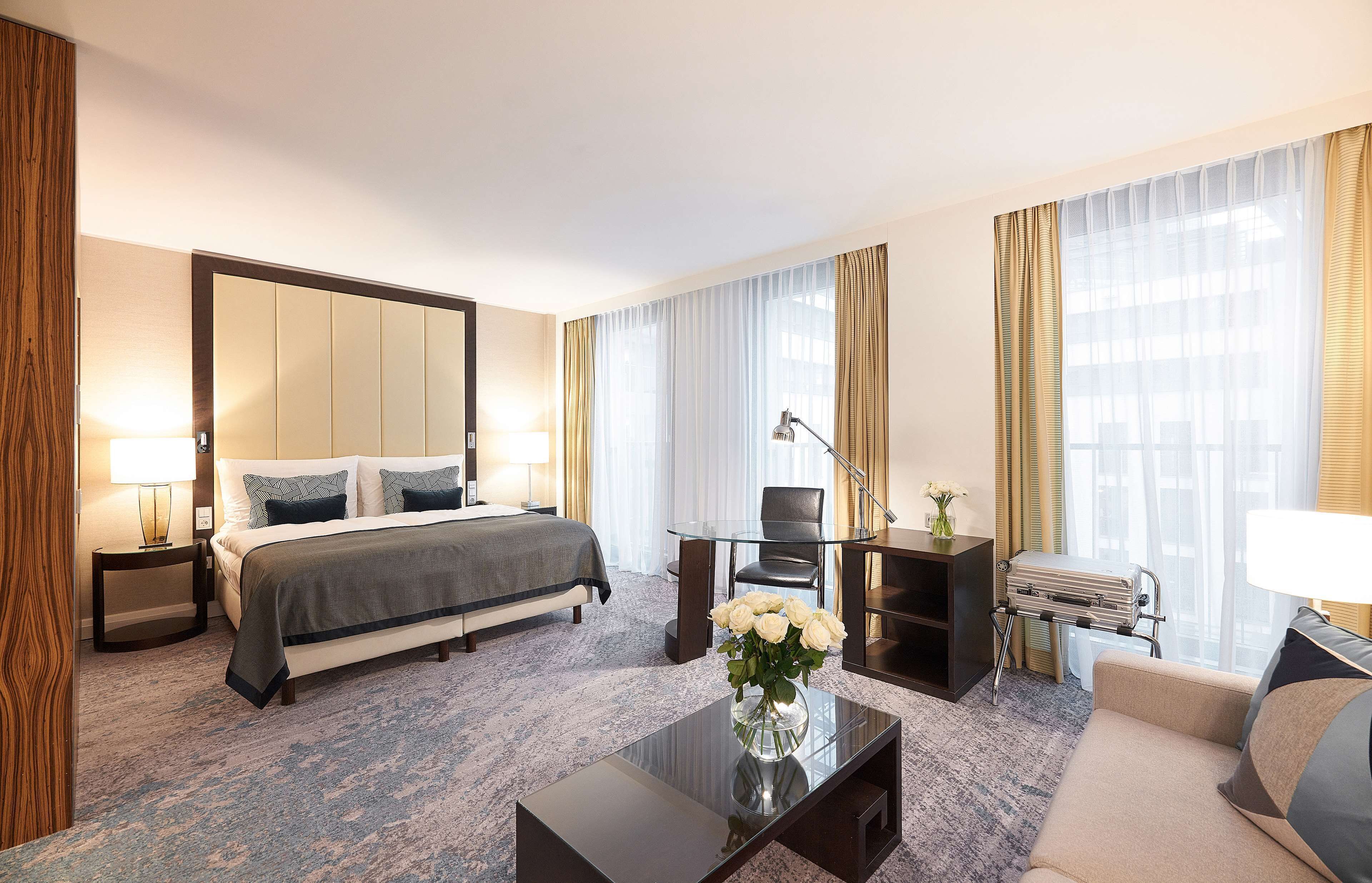 A hotel room with a bed, a desk, a chair, a coffee table, and a lamp.