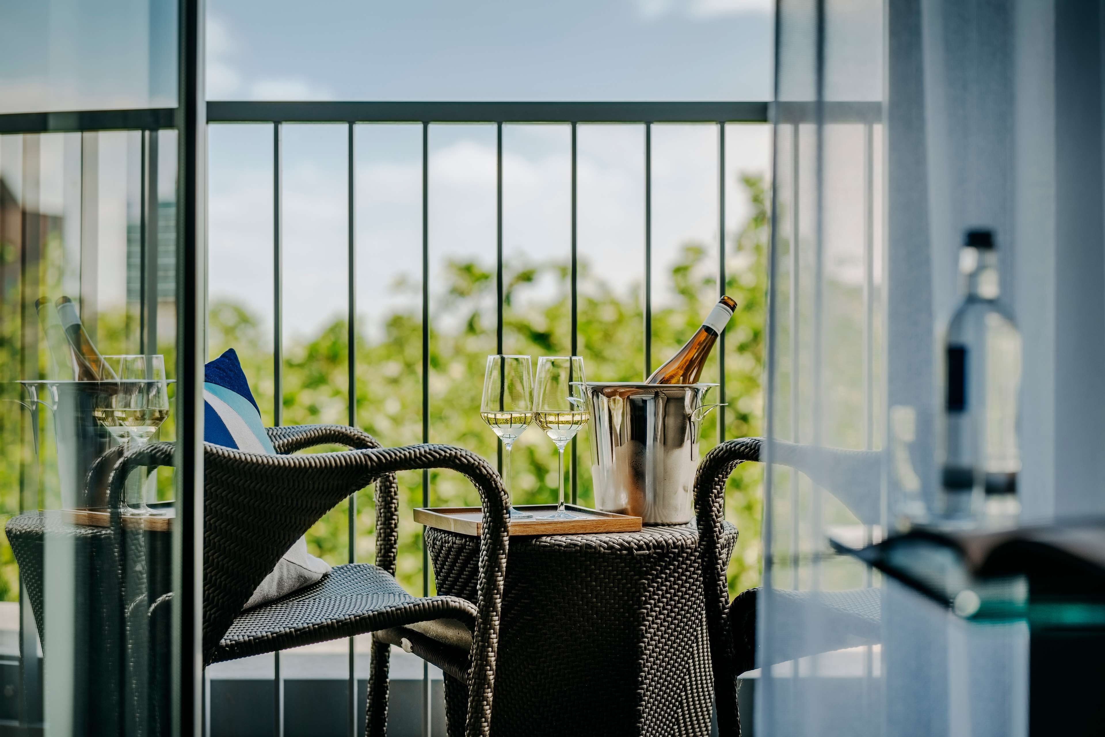 Un balcon avec des fauteuils en osier, une table et une bouteille de champagne.