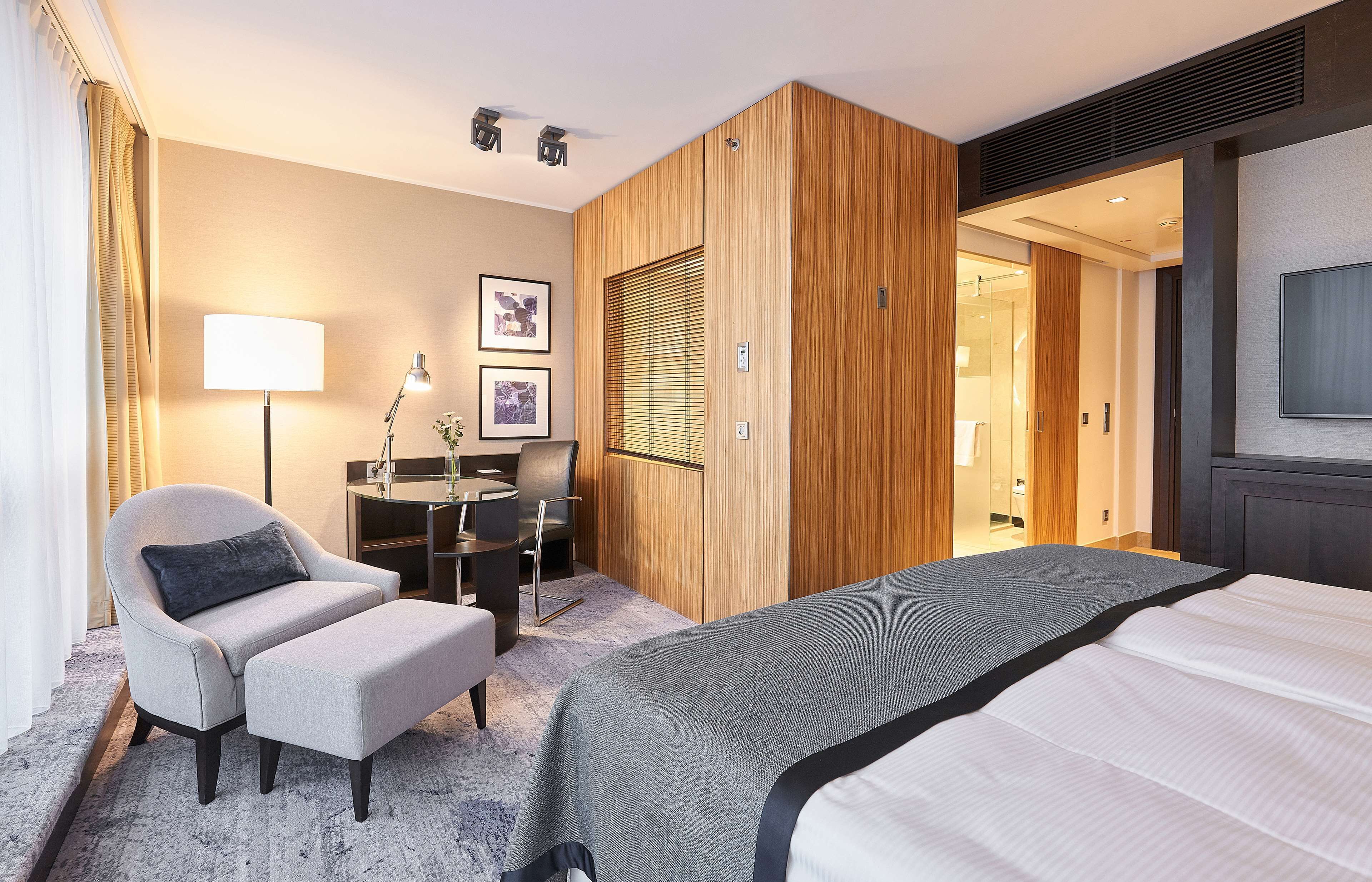 A modern hotel room with a large bed, a desk with a chair, a sofa, and a TV.