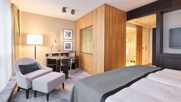 A modern hotel room with a large bed, a desk with a chair, a sofa, and a TV.