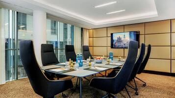 A conference room with a long table, six chairs, and a television screen on the wall.