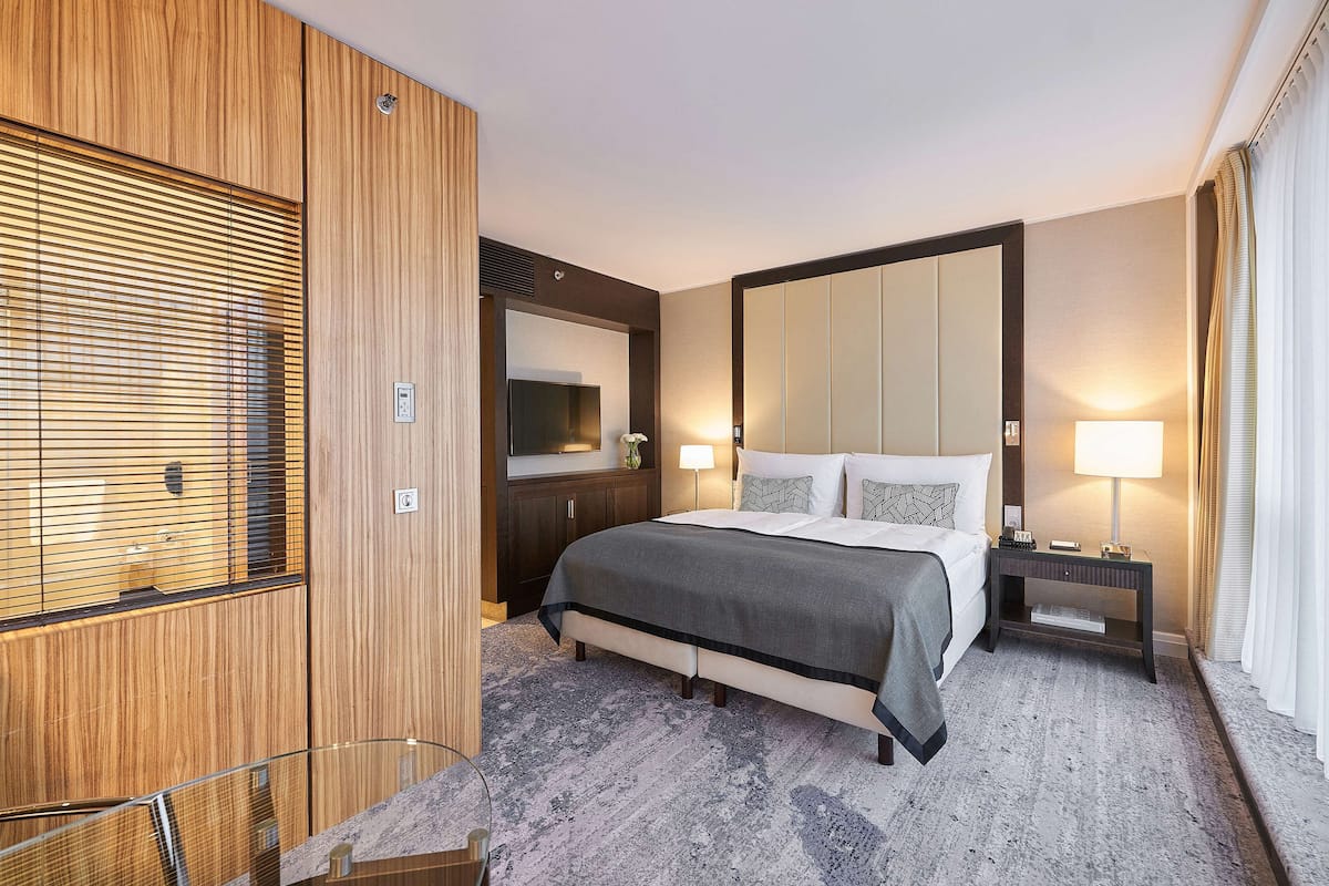 A hotel room with a large bed, a bedside table with a lamp, a wooden wardrobe, and a large mirror on the wall.