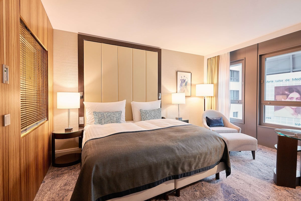 A hotel room with a large bed, two bedside tables with lamps, a chair, and a window with curtains.