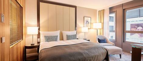 A hotel room with a large bed, two bedside tables with lamps, a chair, and a window with curtains.