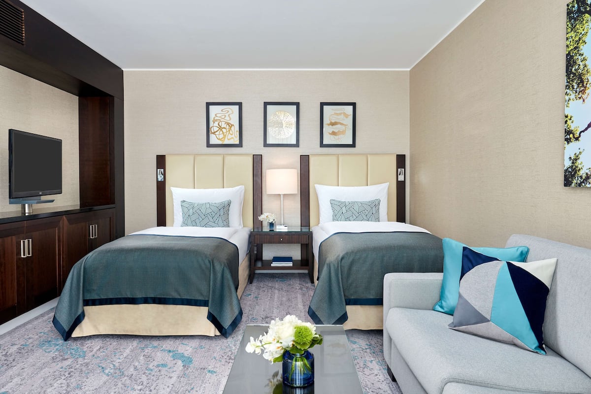 A hotel room with two beds, a sofa, a TV, and artwork on the walls.
