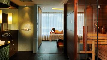 Relax in a serene space with a large bed, glass partition, and a spacious bathroom featuring a sink and mirror.