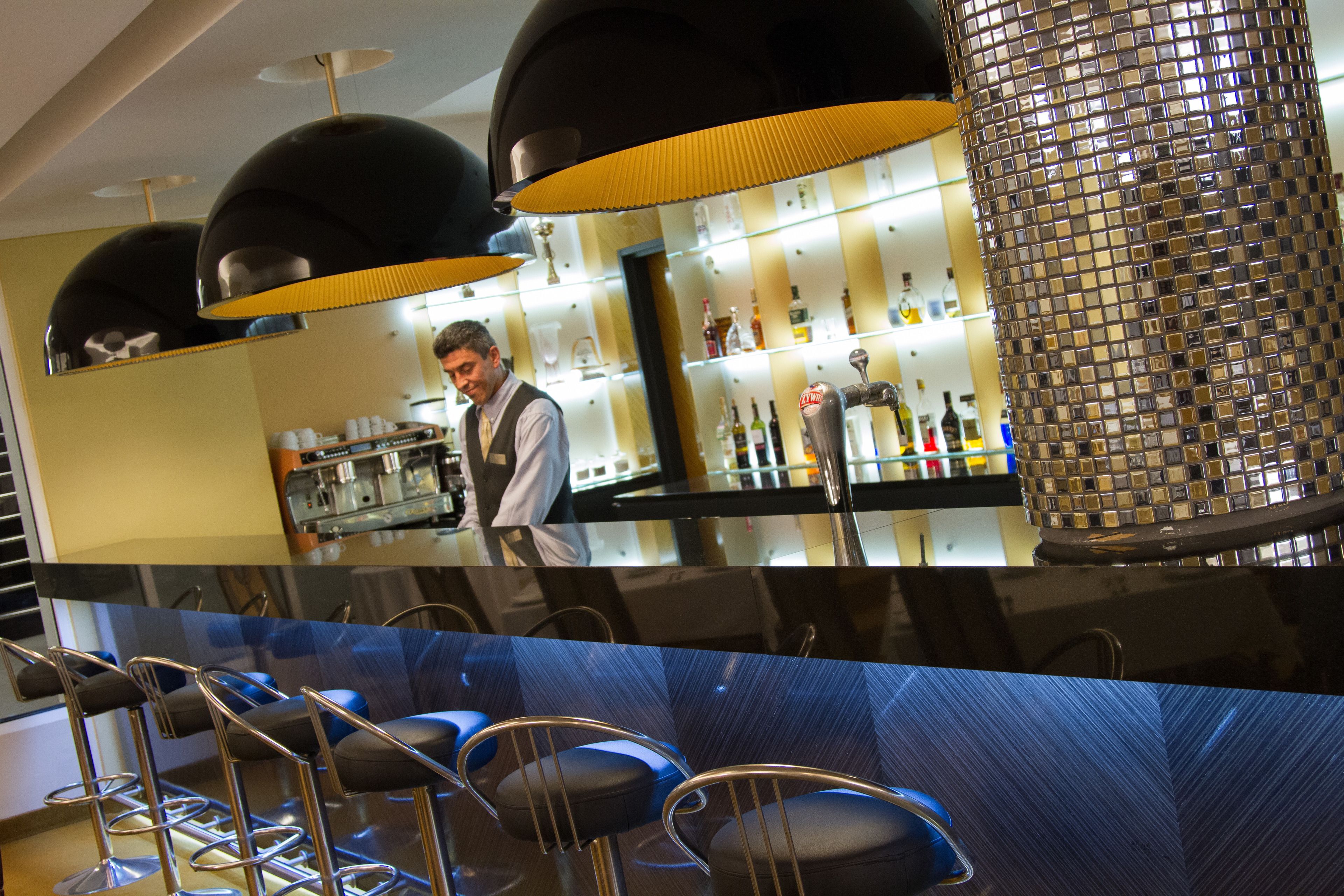 Un espace bar avec un barman, des tabourets de bar et une colonne recouverte de miroirs.