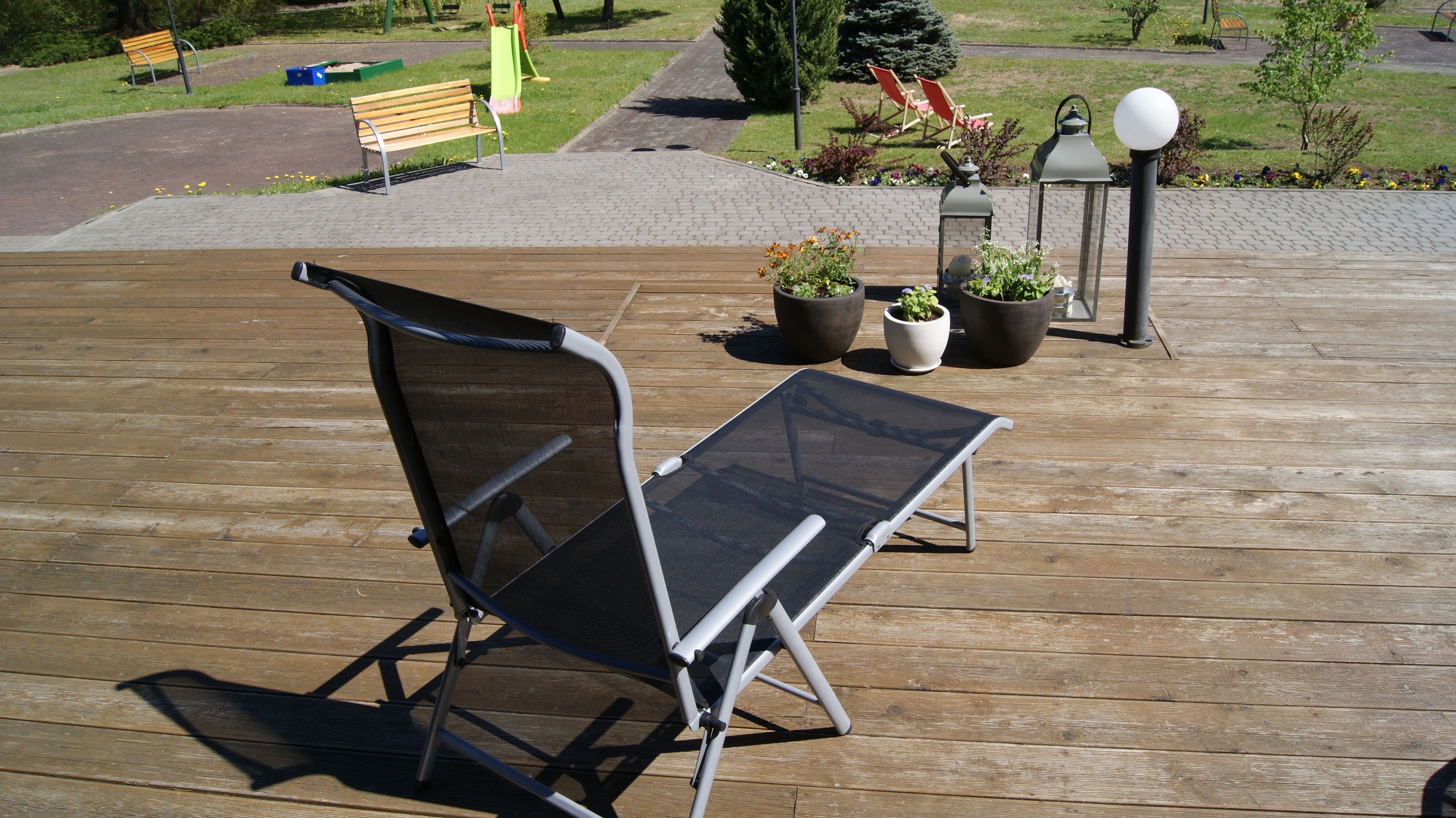 Una terraza de madera con una silla plegable y plantas en macetas.
