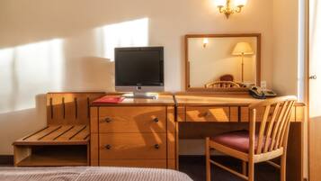 A hotel room with a wooden desk, a computer, a chair, a bed, and a mirror.