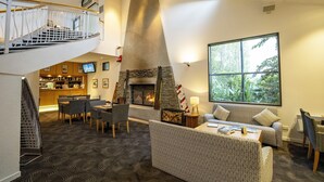 A spacious living area with a fireplace, comfortable seating, a bar area, and a staircase leading to an upper level. - Scenic Suites Queenstown (Queenstown)