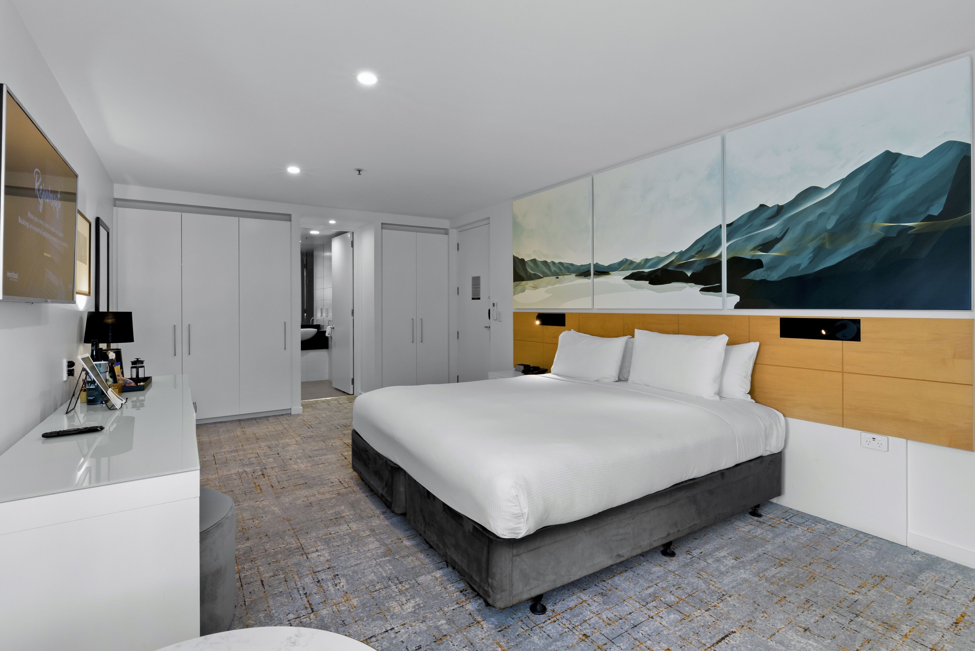 Een moderne hotelkamer met een groot bed, een bureau en een schilderij van bergen aan de muur.