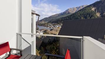 A balcony with a view of a lake and mountains, featuring red chairs and a glass railing.