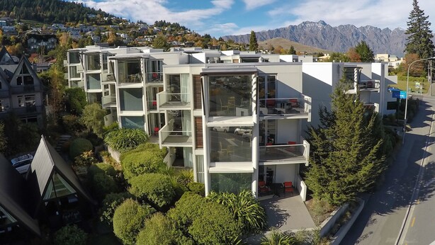 A modern multi-story residential building with balconies, surrounded by greenery and a mountainous backdrop. - Scenic Suites Queenstown (Queenstown)