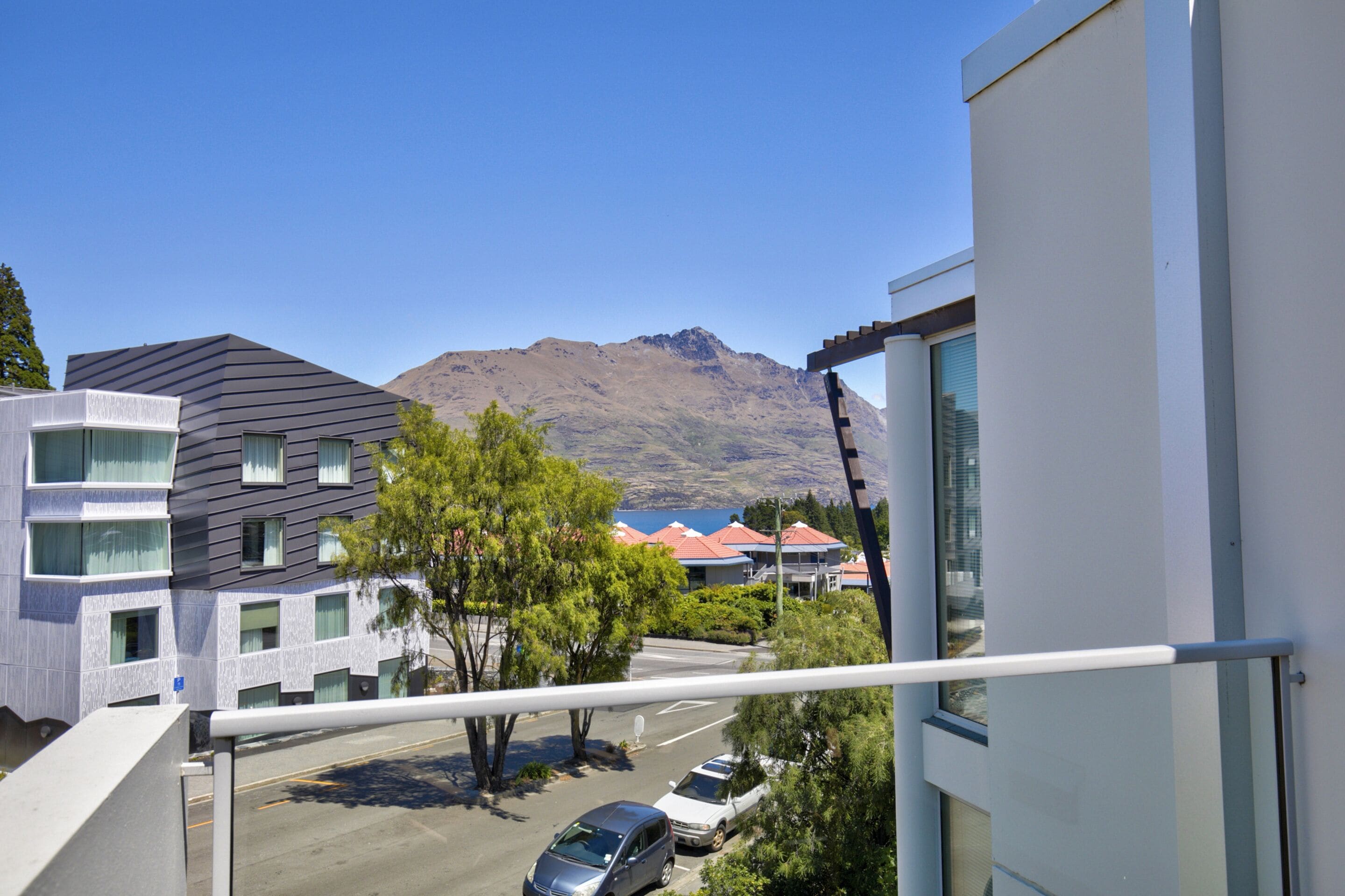 A modern building with a balcony overlooking a parking area and a mountain in the background.