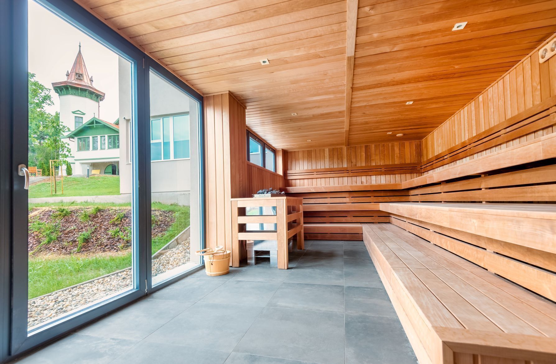 Un sauna avec des bancs en bois et une vue sur un bâtiment doté d’un toit végétalisé.