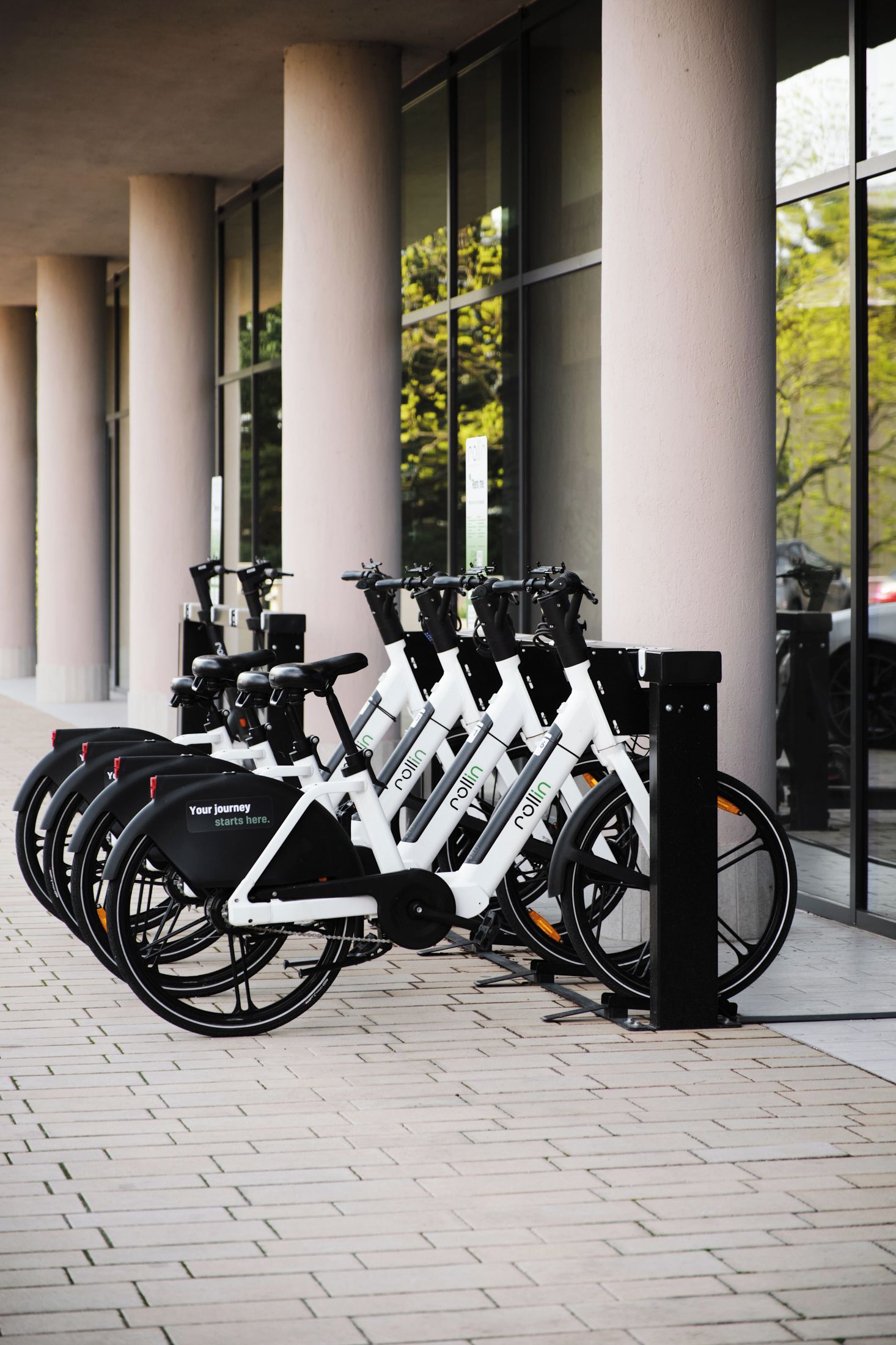 Una fila de bicicletas estáticas estacionadas frente a un edificio con grandes ventanales.