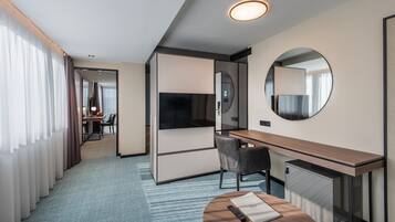 Hotellihuone, jossa on työpöytä, tuoli, televisio ja pyöreä peili.