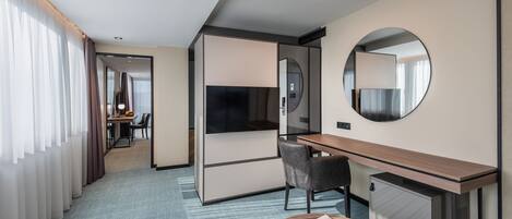 Habitación de hotel con escritorio, silla, televisión y un espejo redondo.