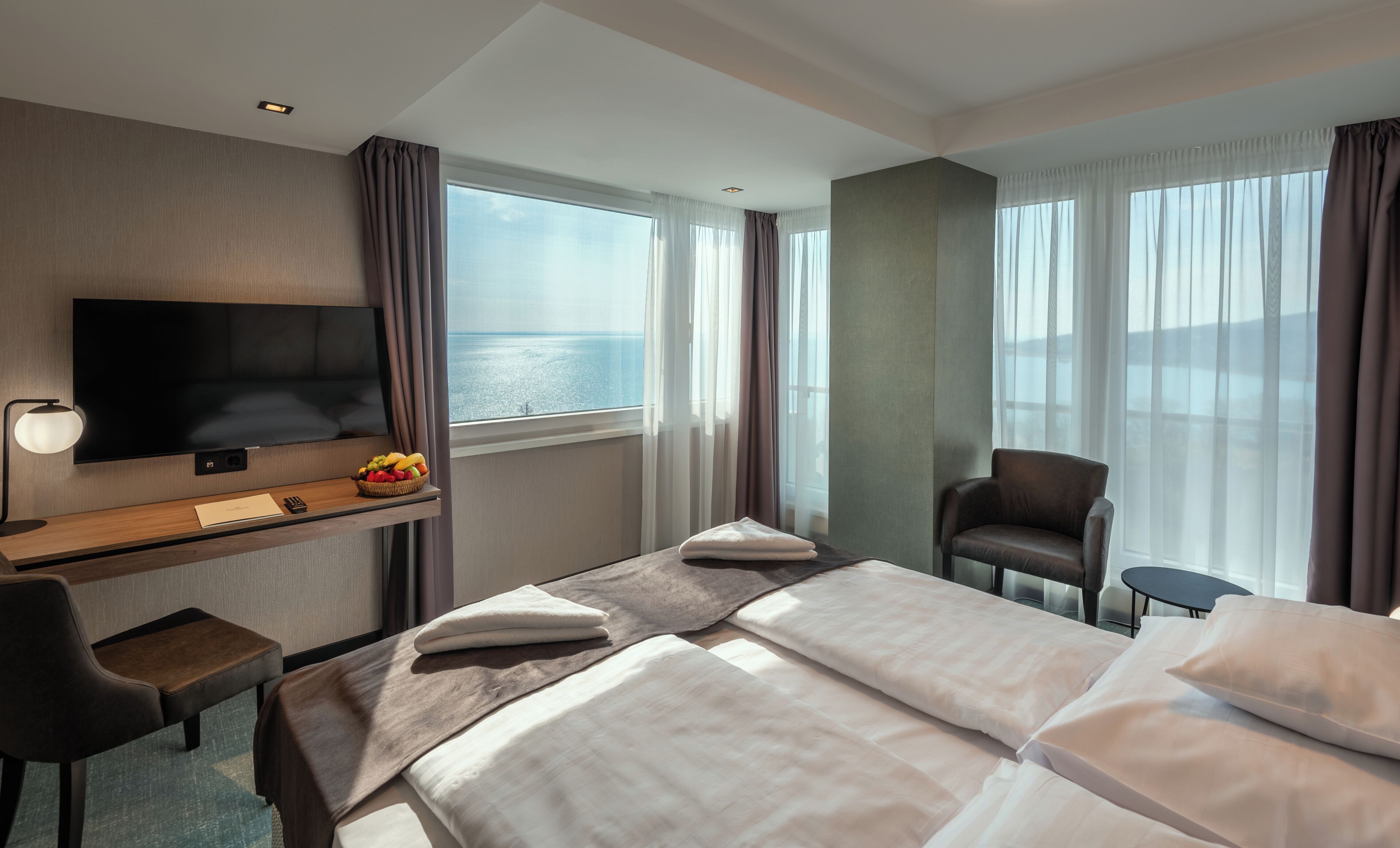 Habitación de hotel con cama, escritorio con televisor, una silla y vista al mar.