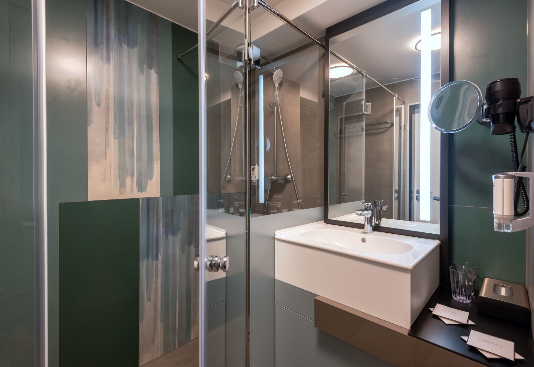 Un baño moderno con cabina de ducha de vidrio, un espejo grande y un secador de pelo montado en la pared.