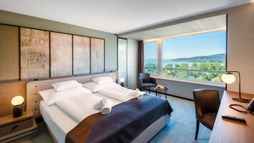 A hotel room with a large bed, a desk, a chair, and a view of the landscape.