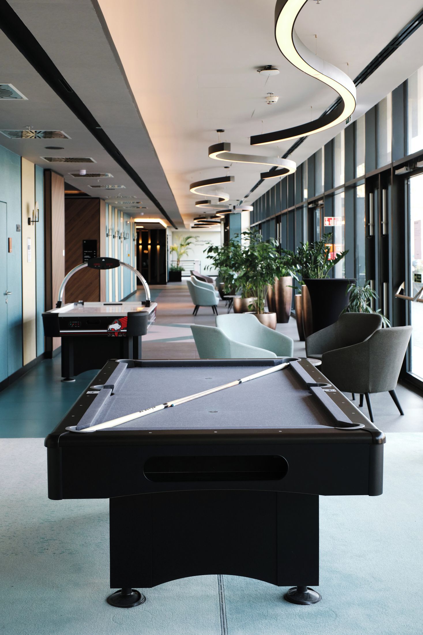 A pool table in a modern indoor setting with seating and large windows.