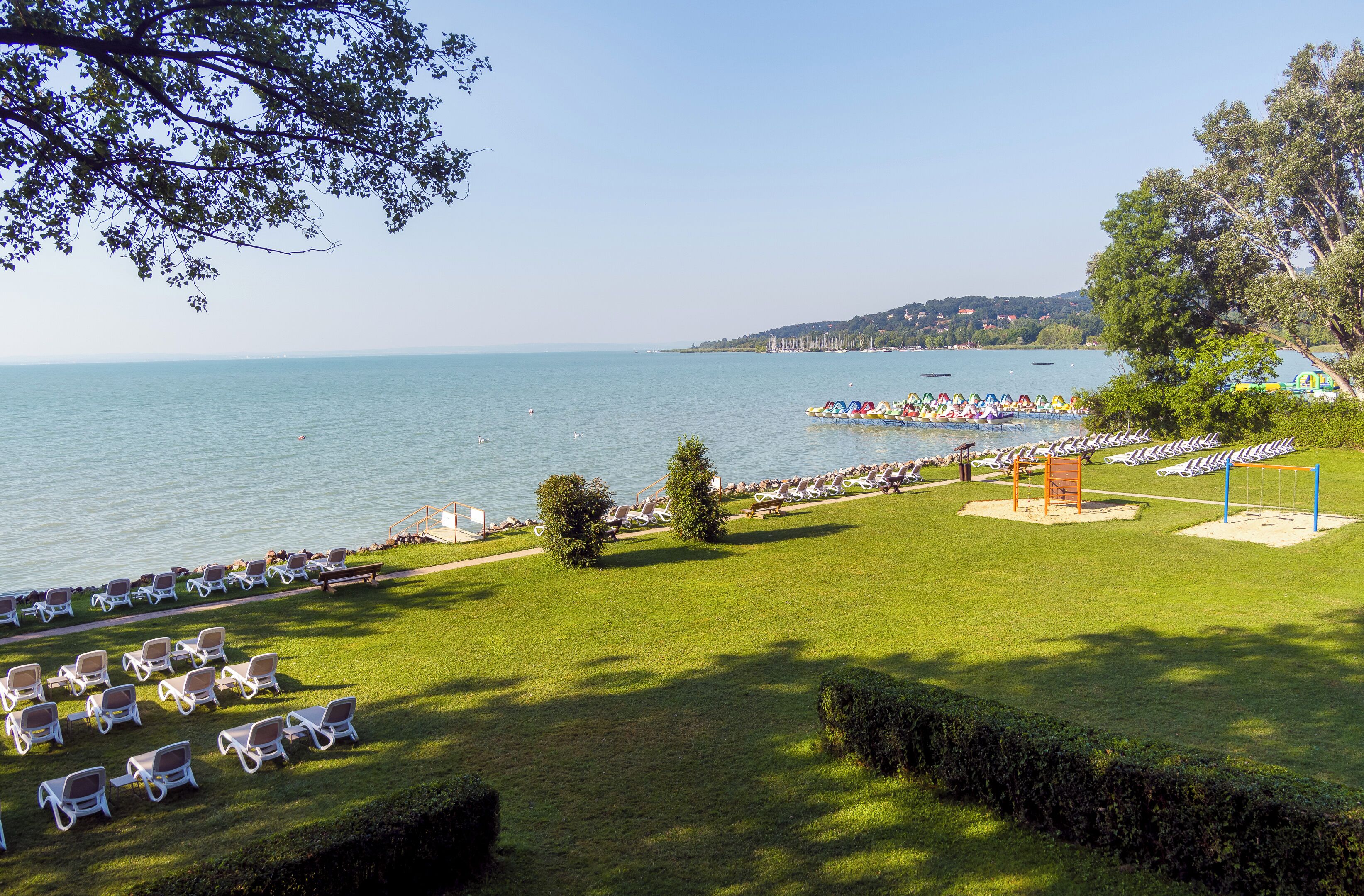 A coastal view with a grassy area, lounge chairs, and a row of colorful boats.