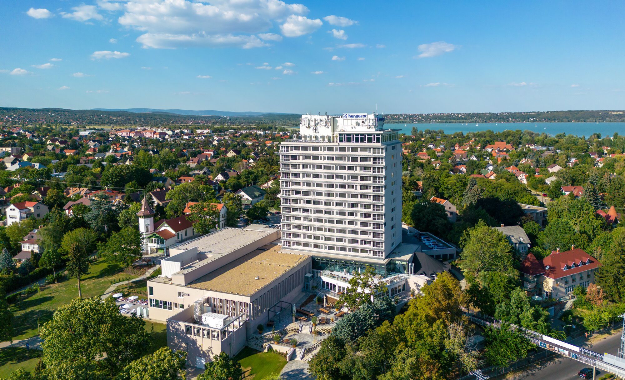 Een hoog hotel met modern design, met een terras op het dak en uitzicht op een meer.