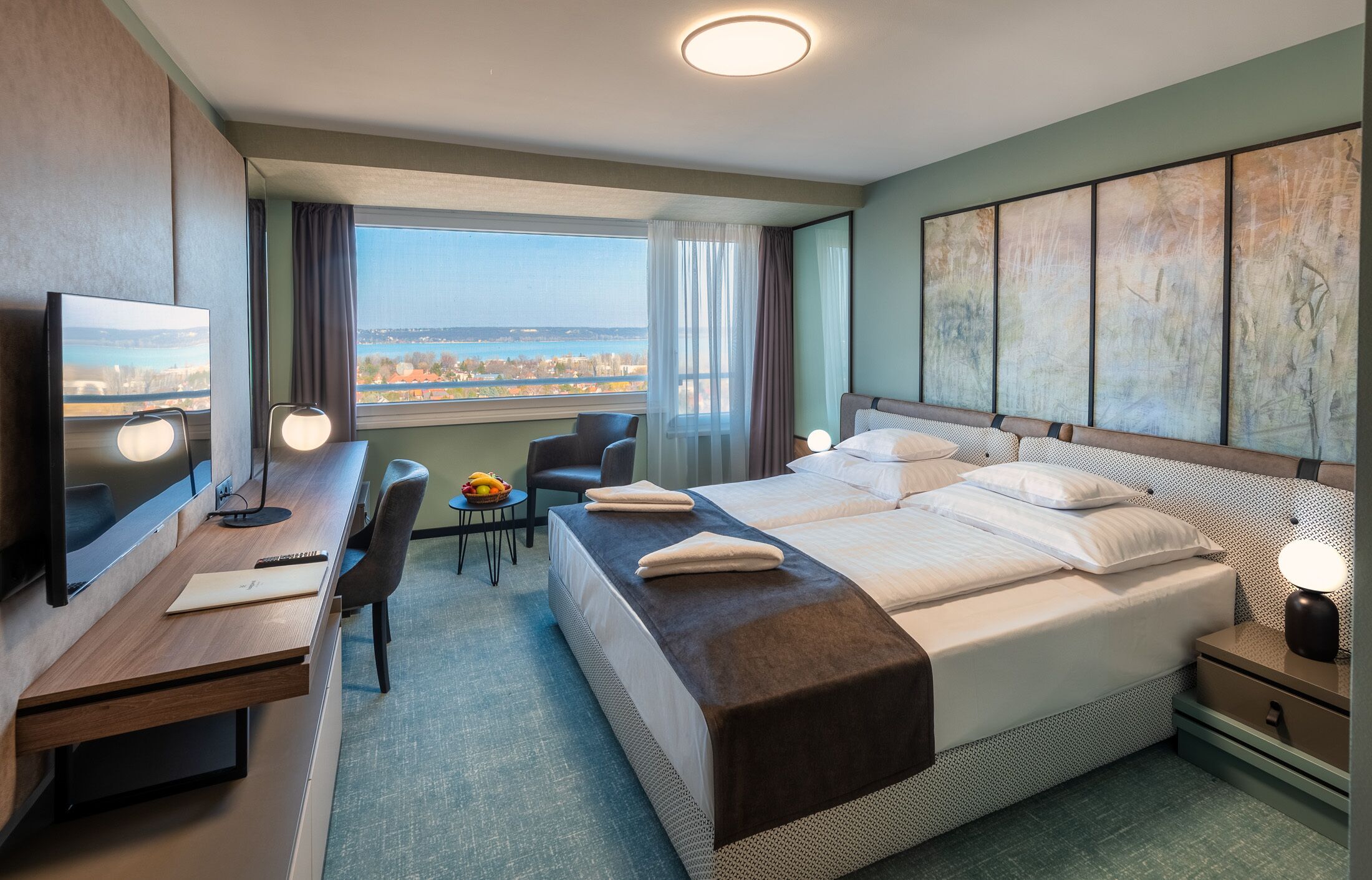 Habitación de hotel con cama, escritorio, silla y una ventana grande con vistas a la ciudad.