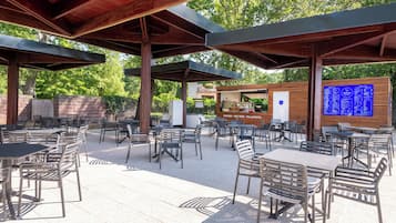 An outdoor patio with metal tables and chairs, a wooden structure overhead, and a menu board in the background.