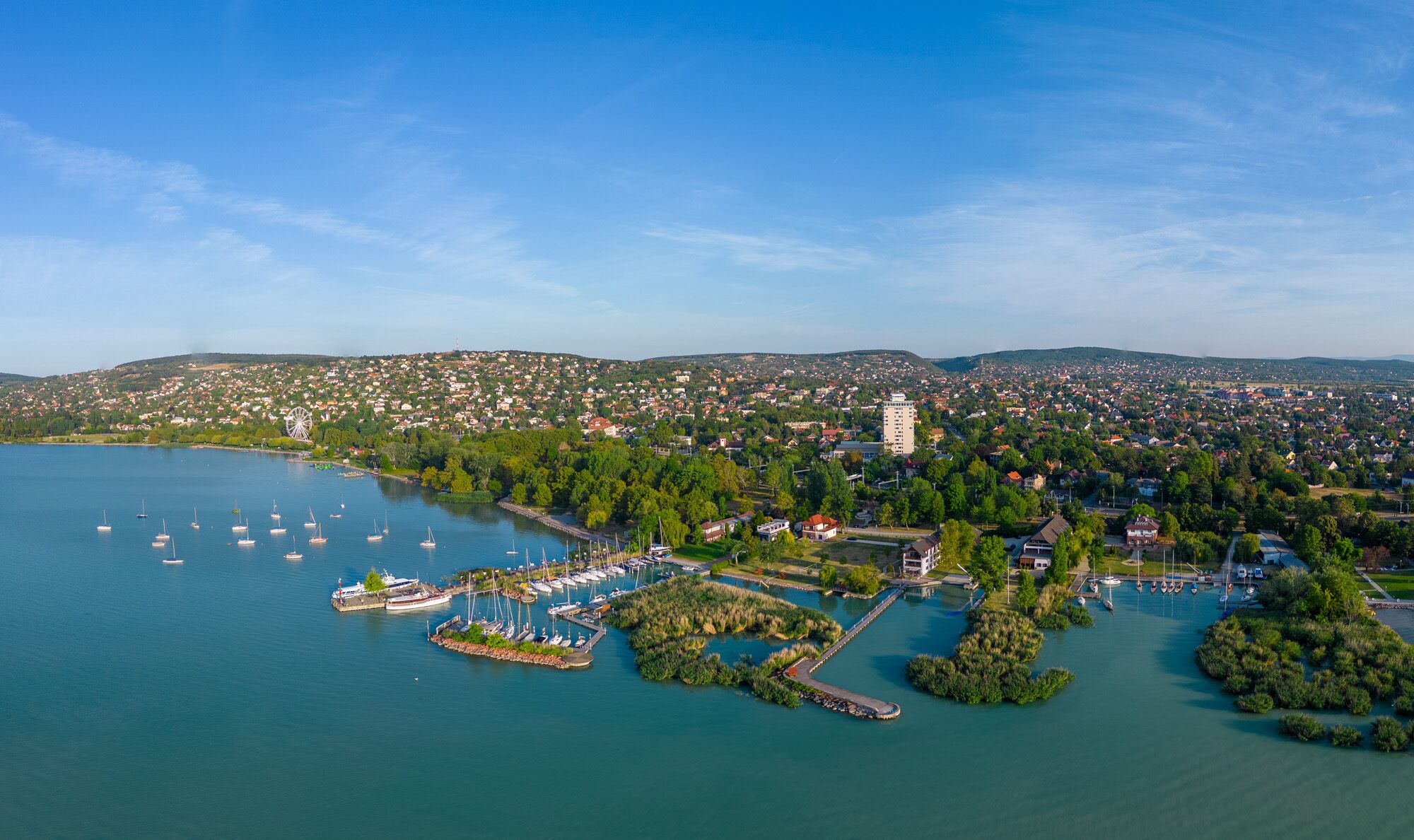 An aerial view of a coastal town with a marina, houses, and a prominent hill in the background.