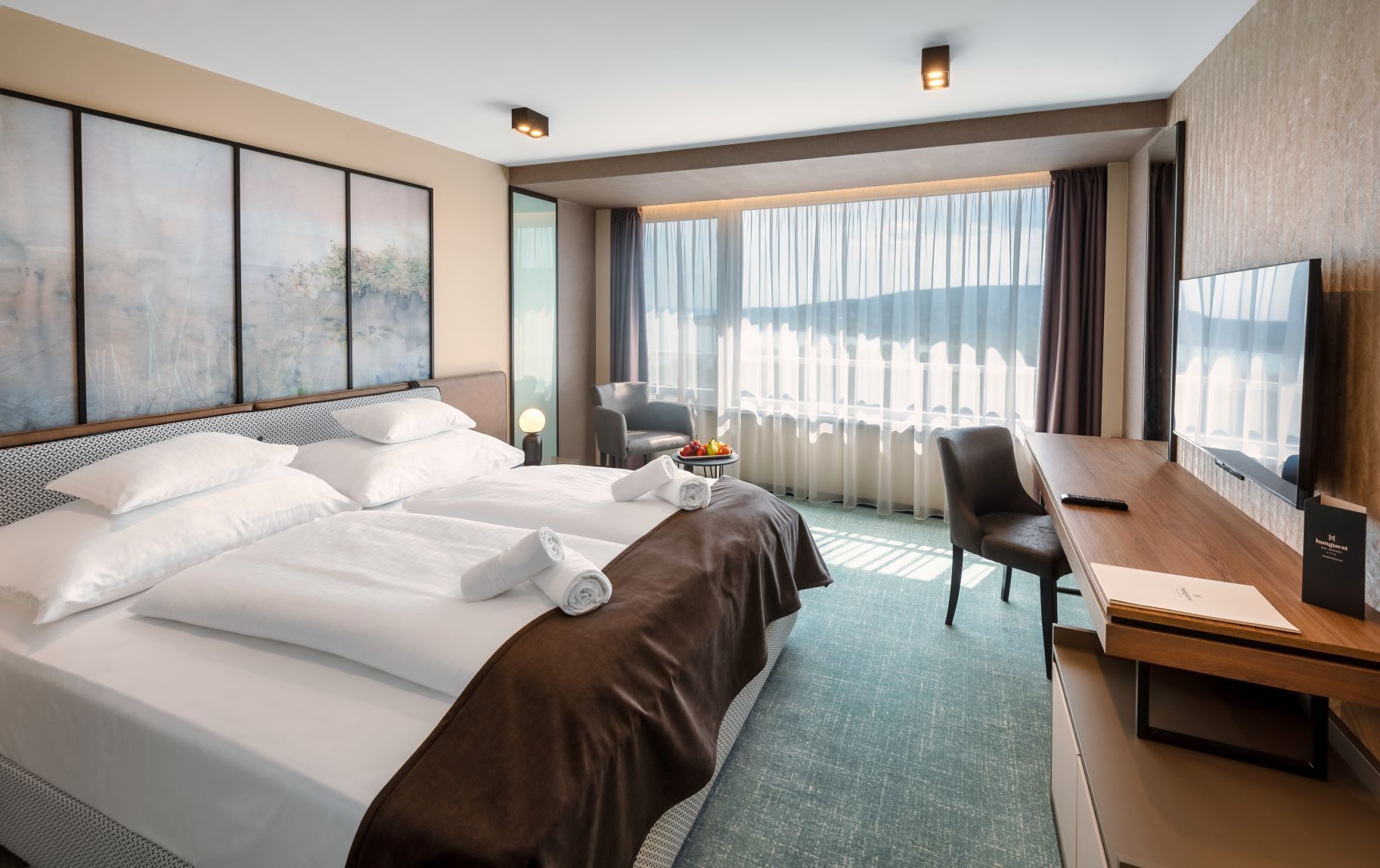 A hotel room with a large bed, a desk, a chair, and a view of the outdoors.