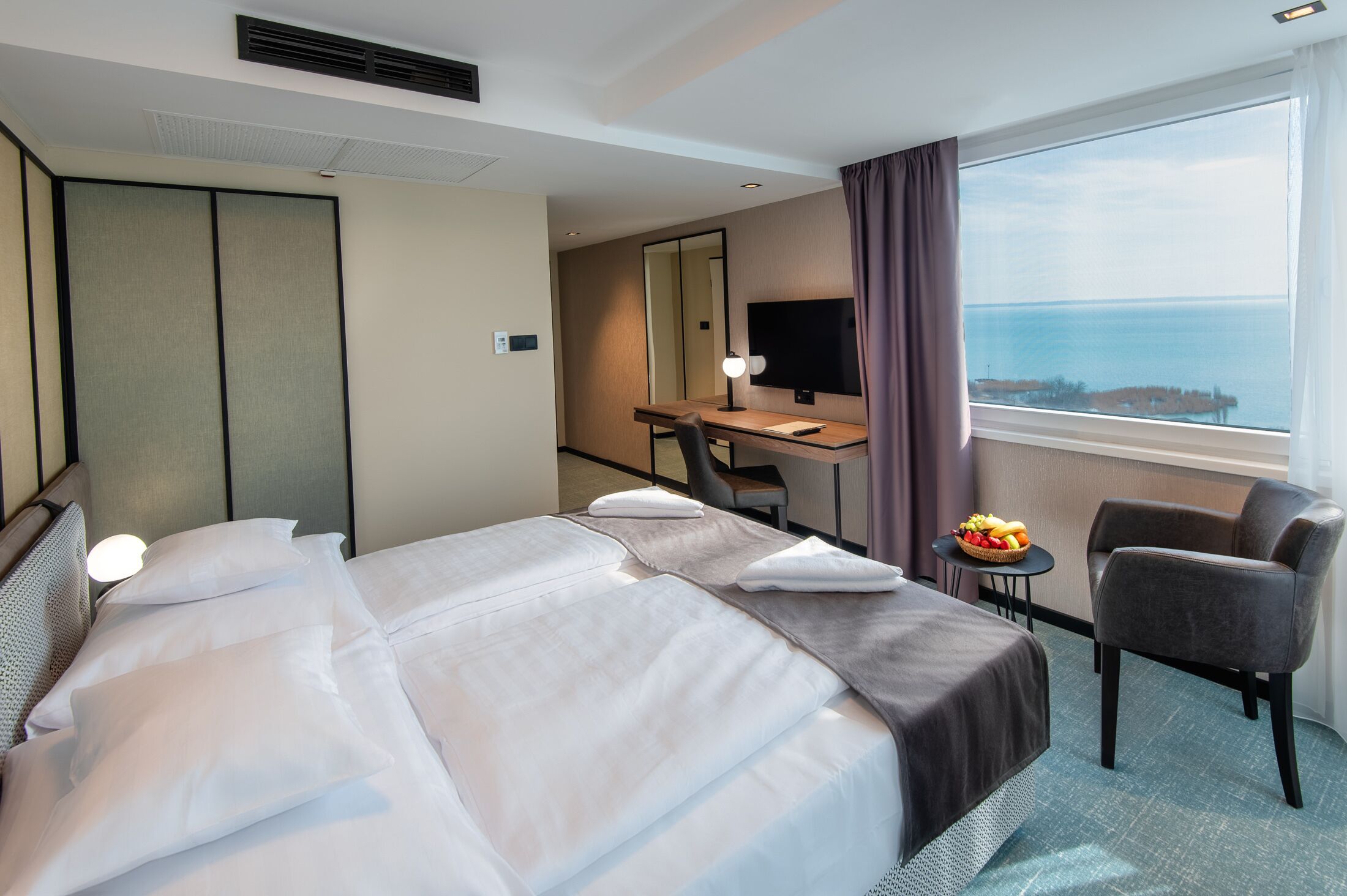 Habitación de hotel con una cama grande, un escritorio, una silla, un televisor y vista al mar.