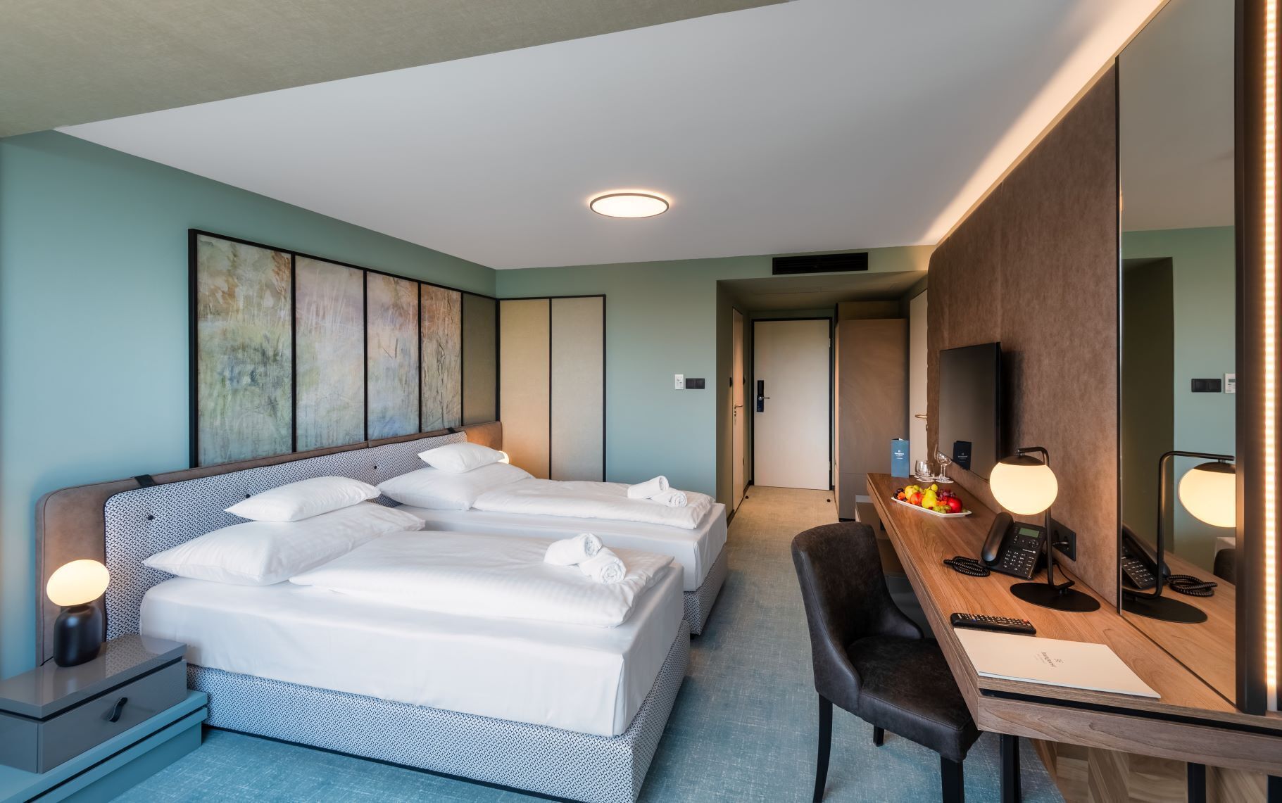 A hotel room with a large bed, a desk with a computer, a chair, and a mirror.